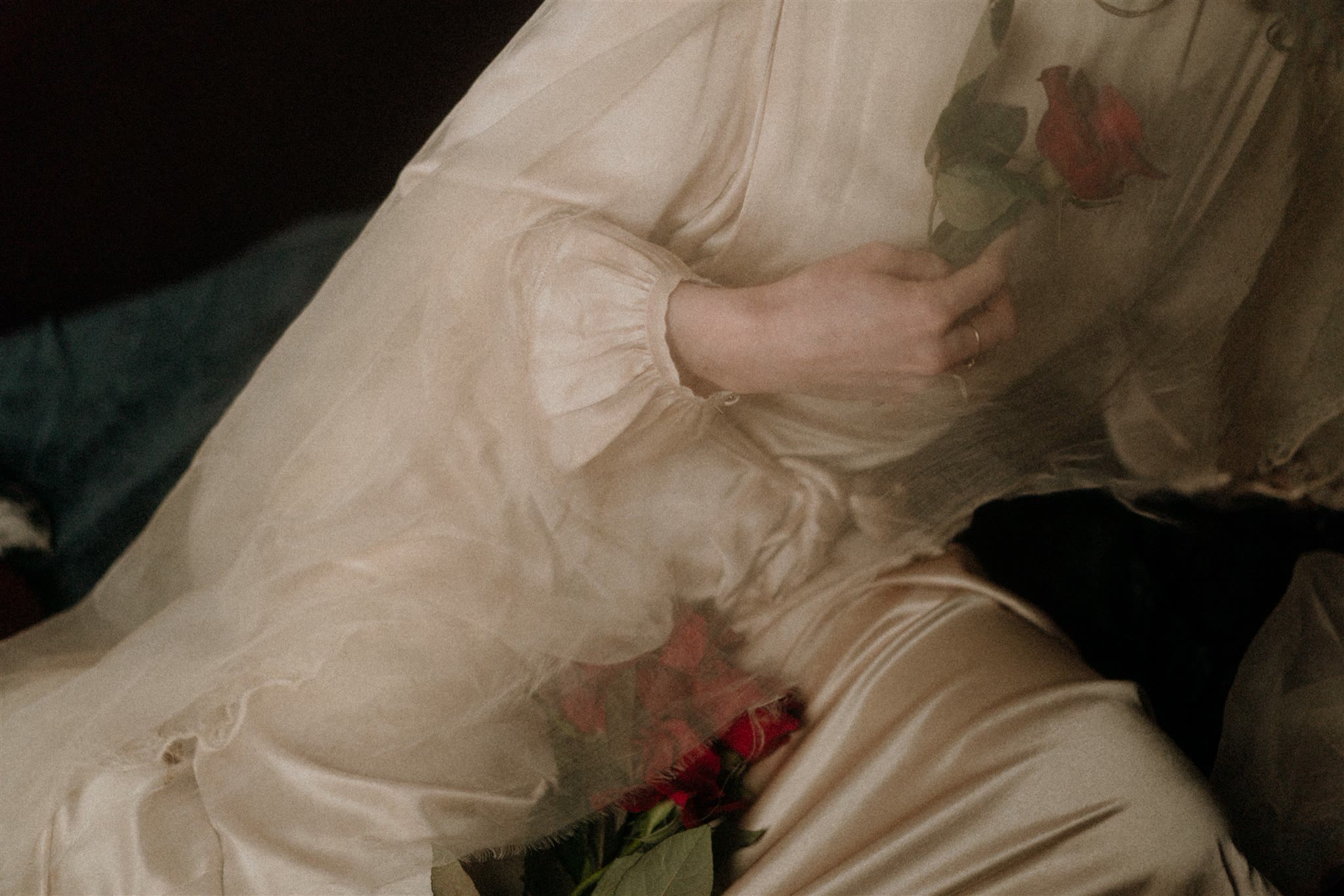 Hände in einem Seidenkleid halten rote Rosen